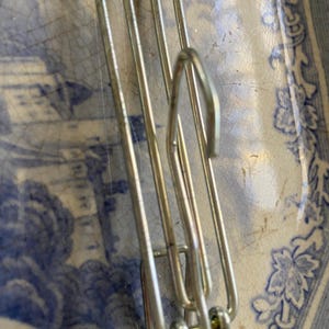 May include: A silver metal curtain tieback with four prongs and a hook. The tieback is designed to hold curtains or drapes in place.
