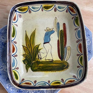 May include: Hand-painted, square ceramic serving dish with a border of colorful, stylized floral and geometric designs. The center features a figure in a sombrero, blue shirt, and white pants, with cacti and other desert plants.