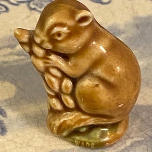 May include: A brown ceramic figurine of a squirrel sitting on a branch, holding a nut in its paws. The figurine is made by Wade and has a green base.