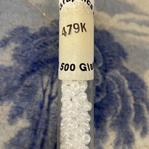May include: A small glass tube filled with white seed beads. The tube has a label that reads "Graphics 479K 500 Glass".