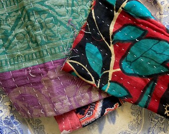 May include: A stack of colorful fabric scraps with different patterns, including floral, geometric, and paisley designs. The fabric is a mix of red, green, purple, and black.