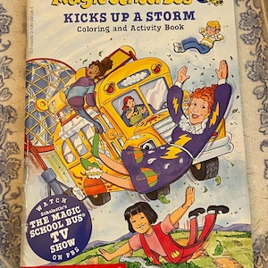May include: A yellow school bus with a smiling face flies through the air with a girl holding an umbrella. The bus is surrounded by clouds and raindrops. The book cover features the title "The Magic School Bus Kicks Up A Storm" and is a coloring and activity book. Watch the TV show on PBS.