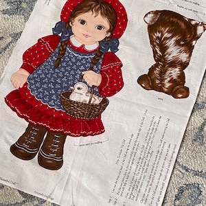 May include: A fabric panel for a DIY doll project featuring a printed illustration of a girl in a red bonnet and blue dress holding a basket with a chick. The panel includes printed sewing instructions, a brown animal back piece, and the text "Amanda and Rags" and "Beautiful Doll" by V.I.P. screen print Cranston Print Works Co.