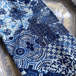 Peut inclure: Tissu plié avec un motif patchwork dans les tons de bleu et blanc. Le tissu présente divers motifs, notamment floraux, géométriques et des motifs de type cachemire. Le tissu est probablement en coton ou dans une matière similaire.