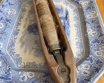 May include: A wooden bobbin with a spool of natural fibre thread inside. The bobbin is resting on a blue and white floral patterned plate.