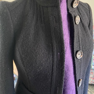 May include: A black wool jacket with a purple lining and button closures. The jacket has a stand-up collar and long sleeves.