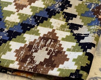 May include: Close-up of a folded fabric with a geometric pattern. The design features a repeating diamond pattern in shades of brown, green, blue, black, and white. The fabric appears to be a woven material, possibly for upholstery or home decor.