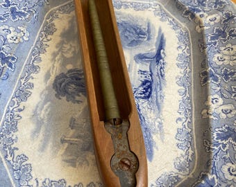 May include: A wooden shuttle with a metal tip and a green bobbin inside. The shuttle is lying on a blue and white floral patterned plate.