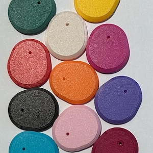 May include: A collection of eleven irregularly shaped, flat, circular pendants in various solid colors including yellow, green, white, magenta, red, orange, purple, black, light pink, teal, and dark red, each featuring a single small hole near the top.