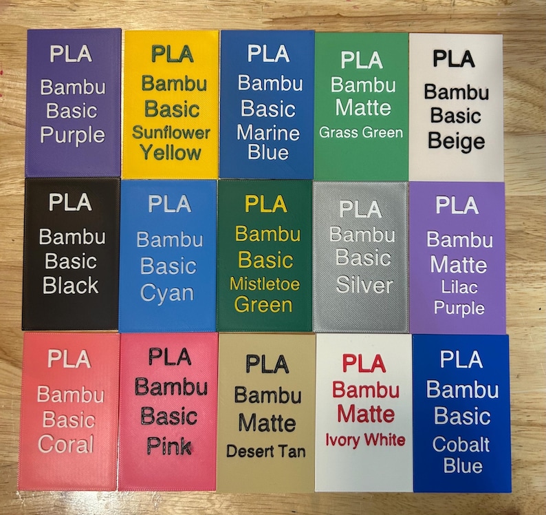 May include: A grid of fifteen rectangular PLA filament sample swatches in various colors including purple, yellow, blue, green, beige, black, cyan, silver, lilac, coral, pink, tan, white, and cobalt, each labeled with its specific color name.