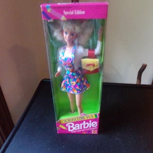 May include: A Special Edition Barbie doll in its original packaging. The doll is wearing a colorful dress and carrying a yellow purse. The box is pink and green with the words "Schooltime Fun" and "Barbie" printed on it.