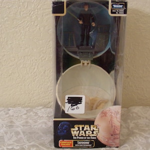 Op de afbeelding: Een Star Wars action figure set met een Tatooine-planeet met een lichtgevend lightsaber. De set bevat een figuur van een Jedi-ridder die een lightsaber vasthoudt.