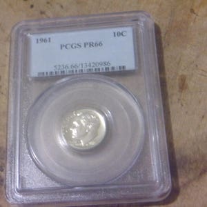 May include: A 1961 10c US dime coin graded PR66 by PCGS in a plastic coin holder. The coin is in excellent condition and has a silver finish.