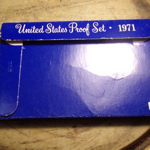 Könnte beinhalten: Blaue Pappbox mit dem Text "United States Proof Set - 1971" auf der Vorderseite. Die Box hat ein weißes Etikett unten rechts mit dem Text "27F".
