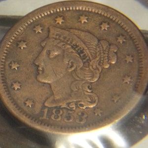May include: A copper-colored coin from 1853, featuring a profile of a woman with the word "LIBERTY" visible. The coin is surrounded by stars and has a detailed edge.