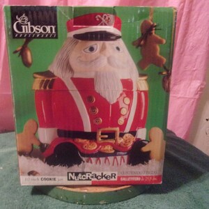 Può includere: Un barattolo per biscotti in ceramica rosso e bianco alto 25 cm a forma di schiaccianoci. Il barattolo ha una bordatura dorata e una cintura nera con fibbie dorate. Il barattolo è nella sua confezione originale, che presenta un omino di pan di zenzero e il testo "Nutcracker Contenitore Frigoz Gallettero dl 2.25 kg."