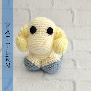 May include: A crocheted stuffed animal shaped like a sheep with yellow ears, black eyes, and blue and white feet.