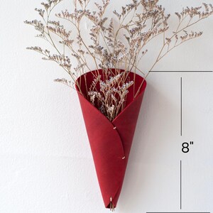 a red cone shaped vase with dried flowers in it