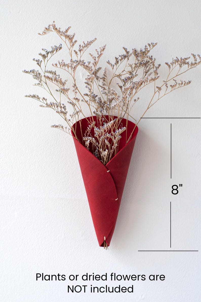 a red cone shaped vase with dried flowers in it