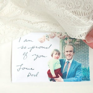 May include: A white card with a handwritten message that says "I am so proud of you Love Dad" and a photo of a man holding a young child.