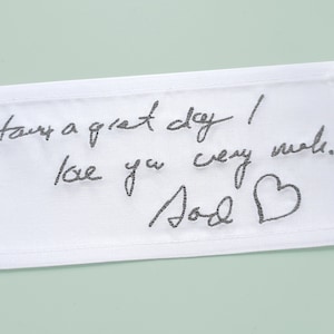Könnte beinhalten: Weißer Stoff mit schwarzem handschriftlichem Text, der "Have a great day! Love you very much. Jord" mit einem kleinen Herzen neben der Unterschrift sagt.