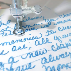 May include: Close-up of a sewing machine embroidering a white fabric with blue thread. The text "Beautiful Philosa, you changed my memories to cherish, you are all grown up, a new chapter is always more" is embroidered on the fabric.