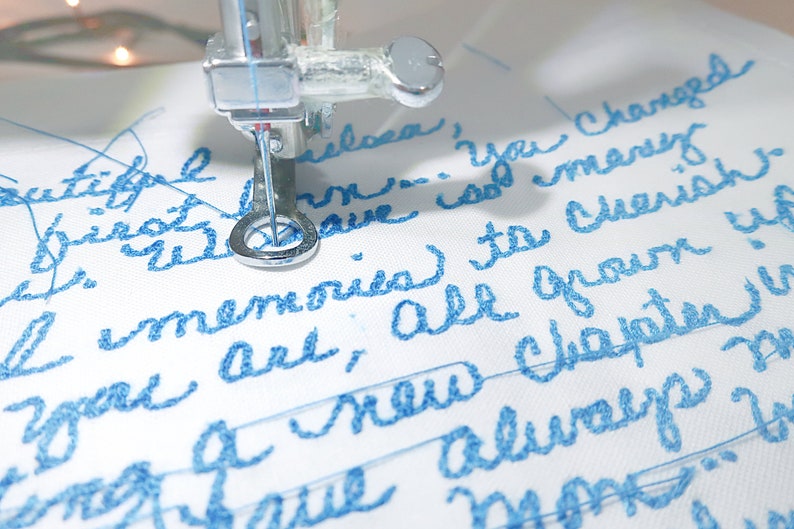 May include: Close-up of a sewing machine embroidering a white fabric with blue thread. The text "Beautiful Philosa, you changed my memories to cherish, you are all grown up, a new chapter is always more" is embroidered on the fabric.