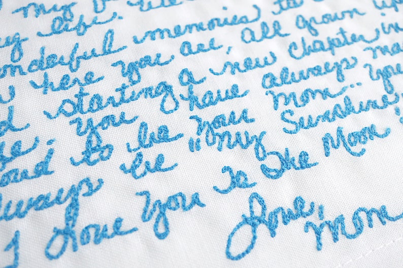 May include: A white fabric with blue embroidery that reads "My life is full of wonderful memories, here you are, all grown up, starting a new chapter in your life. You have always been my sunshine, you are the moon. I love you forever, Mom."