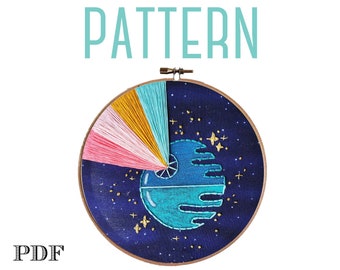 May include: A PDF pattern for a colorful embroidery hoop featuring a blue and turquoise Death Star with a pink, yellow, and blue starburst behind it. The background is a dark blue with gold stars.