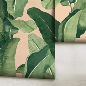May include: A close-up of a wallpaper with a tropical leaf pattern. The leaves are green and have a textured appearance. The background is a light peach color.