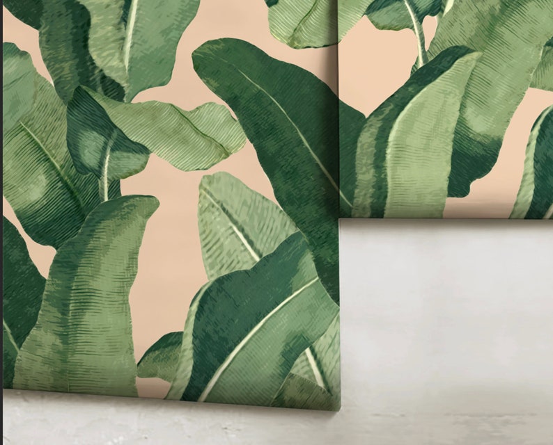May include: A close-up of a wallpaper with a tropical leaf pattern. The leaves are green and have a textured appearance. The background is a light peach color.