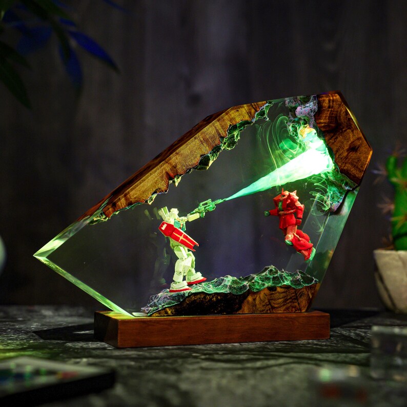 Puede incluir: Una pieza de arte en resina &uacute;nica que presenta dos figuras de robots en una escena de batalla. Las figuras est&aacute;n dentro de un bloque de resina transparente con un marco de madera. La escena est&aacute; iluminada con luz verde, creando un efecto din&aacute;mico.