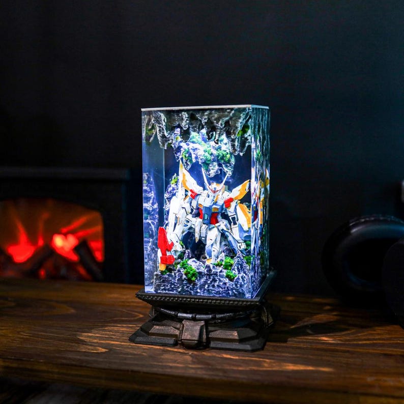 May include: A rectangular, illuminated display featuring a detailed robot model with white, red, yellow, and blue accents. The model is set within a clear, textured enclosure, mounted on a decorative, dark-colored base.
