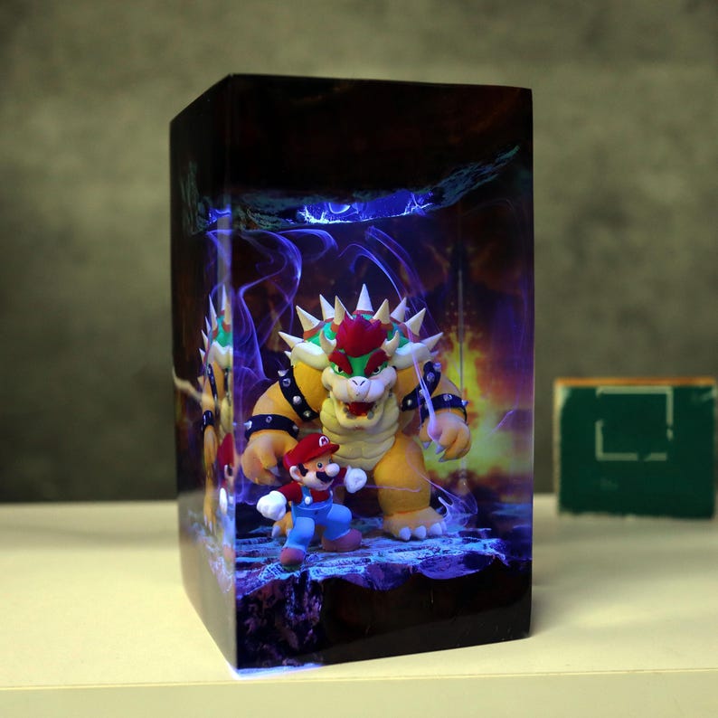 Op de afbeelding: Een rechthoekige, oplichtende display met de personages Bowser en Mario uit de Super Mario-videogame serie. Bowser is een groot, geel, schildpadachtig wezen met een rode hanenkam. Mario is een kleine figuur met een rode hoed en blauwe overall.