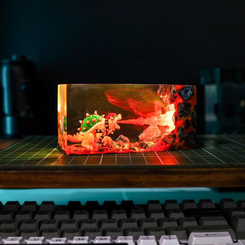 May include: A rectangular resin diorama featuring a Bowser figure breathing fire. The scene includes a lava-filled environment with a detailed, textured rock wall. The diorama is illuminated with red and orange lights, creating a vibrant, dynamic display.