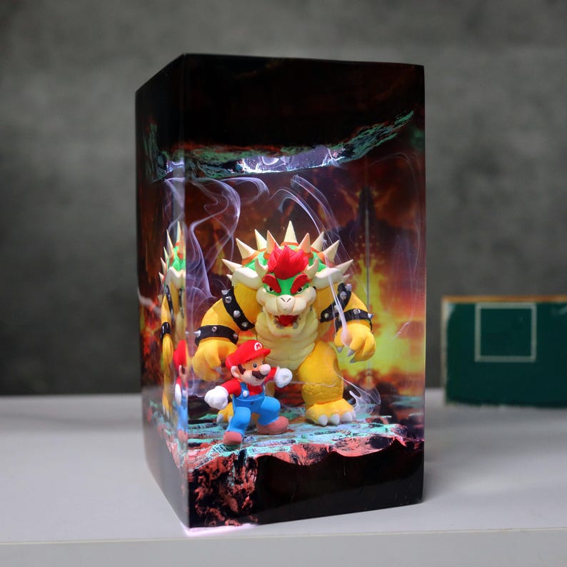 Op de afbeelding: Een rechthoekige, verlichte display met de personages Mario en Bowser uit de Super Mario-videogame serie. Bowser is geel met een rode hanenkam, en Mario draagt zijn klassieke rood-blauwe outfit. De achtergrond toont een vurige sc&egrave;ne.