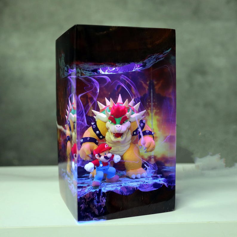 Op de afbeelding: Rechthoekige decoratieve doos met een afbeelding van Mario en Bowser uit de Super Mario-videogameserie. De doos heeft een donkere, getextureerde bovenkant en een gloeiende paarse en oranje achtergrond.