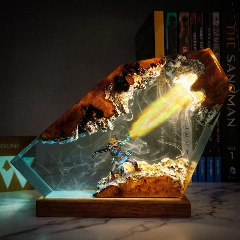 May include: A decorative resin lamp featuring a miniature figure of a character in action, emitting a beam of light. The lamp has a wooden base and a clear, angular resin body with brown and white accents. The scene is illuminated with a warm glow.