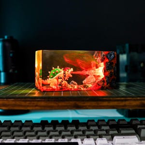 May include: A rectangular resin diorama featuring a Bowser figure breathing fire. The scene is illuminated with red and orange lights, depicting a volcanic landscape. The figure is detailed with a green shell and black studded collar.