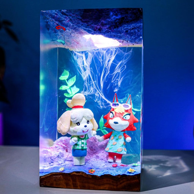 May include: A rectangular resin art piece featuring two cartoon characters in a miniature underwater scene. The scene includes a sandy base, green plants, and a swirling blue and white background. The characters are a white dog and a red fox.