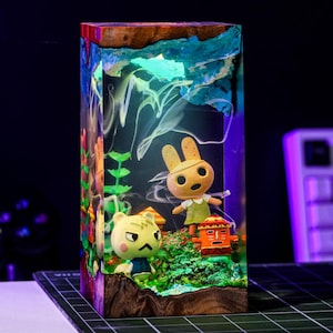 Puede incluir: Una pieza de arte rectangular de resina con personajes de Animal Crossing. La obra de arte tiene una base de madera y un dise&ntilde;o colorido y en capas con una parte superior azul y verde. Los personajes est&aacute;n ambientados en un paisaje en miniatura.