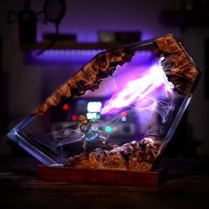 May include: A decorative resin sculpture featuring a miniature figure emitting a beam of purple energy. The sculpture is encased in a clear, geometric form with a wooden base and intricate wood grain details. The energy beam is bright and vibrant.