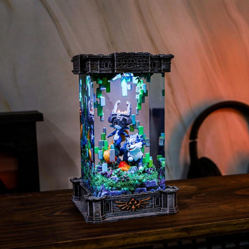 May include: A decorative light-up display featuring two cartoon characters and a wolf-like creature inside a clear rectangular case. The base and top are detailed with a stone-like texture. The scene is illuminated with green and blue pixelated elements.