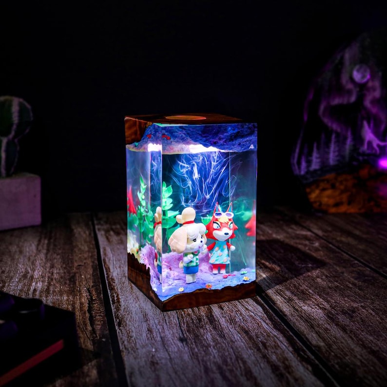 May include: A decorative resin lamp featuring two cartoon characters inside a clear cube. The lamp has a wooden base and a blue and white illuminated interior. The characters are a dog and a fox, both wearing outfits.
