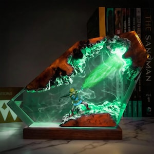 May include: A decorative resin lamp featuring a miniature figure in a dynamic pose, emitting a green energy beam. The lamp has a wooden base and a clear, angled resin body with brown and green accents. The scene is illuminated with green light.
