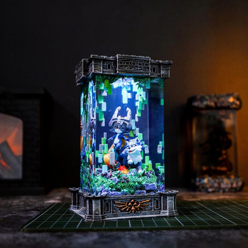 May include: An illuminated resin sculpture with a castle-like top and base, featuring characters from a video game. The rectangular structure contains a detailed scene of a character and a wolf-like creature, surrounded by green pixelated foliage.