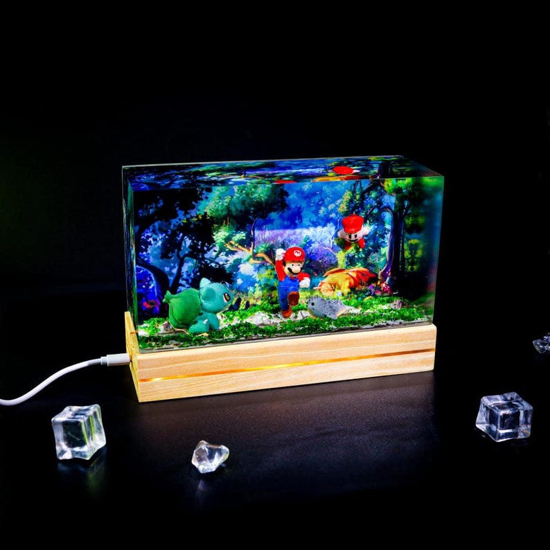 Puede incluir: Una pieza de arte de resina rectangular que presenta una escena de bosque vibrante con Mario, Bulbasaur y otros personajes. La obra de arte est&aacute; iluminada por una base de madera con un brillo c&aacute;lido, y un cable USB est&aacute; conectado. La escena se desarrolla sobre un fondo negro.