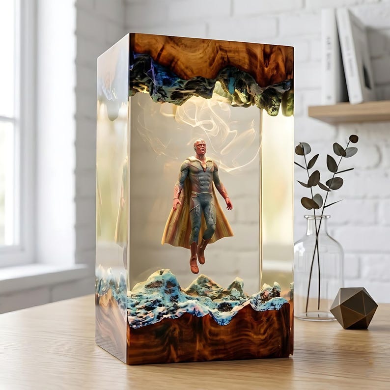 May include: A rectangular resin art piece featuring a superhero figure suspended within. The base and top showcase a wood grain design with blue and brown accents. The figure is wearing a cape and a blue and grey suit.