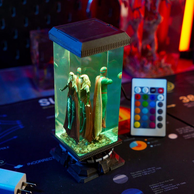 Puede incluir: Una vitrina rectangular iluminada con figuras dentro de un recipiente transparente lleno de l&iacute;quido. La vitrina tiene una parte superior e inferior negras, con un mando a distancia. Las figuras son de color verde, rojo y marr&oacute;n.