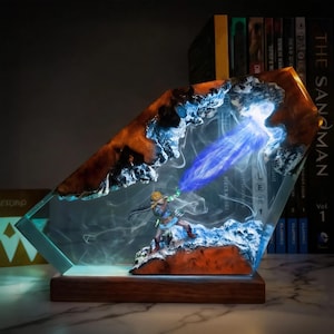 May include: A decorative resin sculpture featuring a miniature figure with a blue energy beam. The sculpture has a wooden base and a clear, angled resin body with orange and blue accents. The figure is in a dynamic pose, suggesting action.